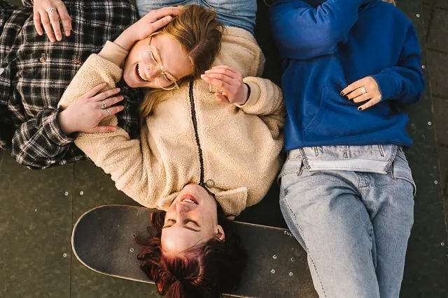 Tre ungdomar som skrattar och ligger på rygg, skateboard.